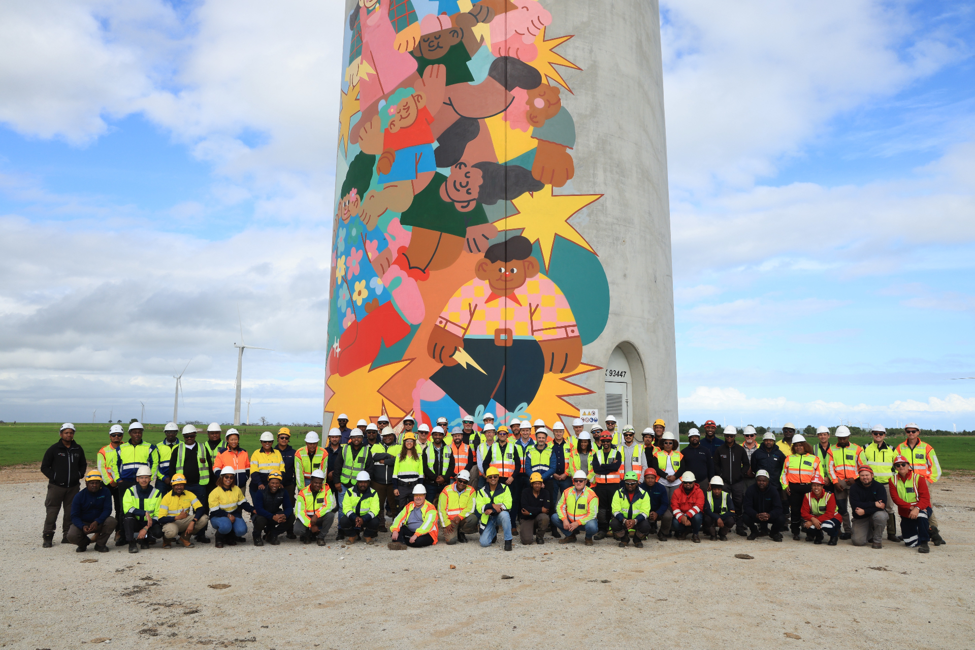 Wind farm project team gathered at the base of a painted turbine tower